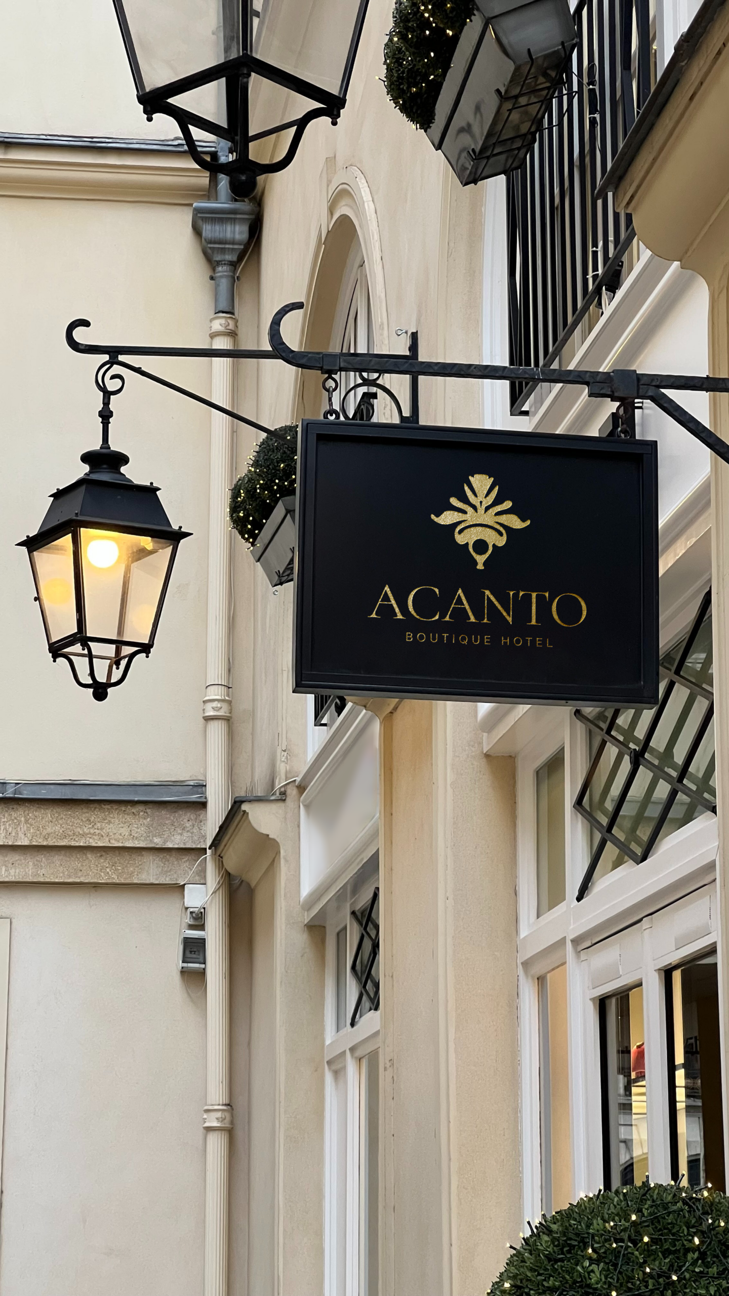 Cartel exterior de ACANTO Boutique Hotel, negro con el logotipo dorado, junto a un farol en una calle
